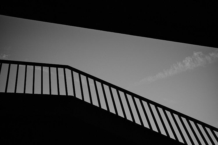 A black and white photo showing the silhouette of a railing against a clear sky. The composition emphasizes clean lines, contrast, and minimalist urban form.