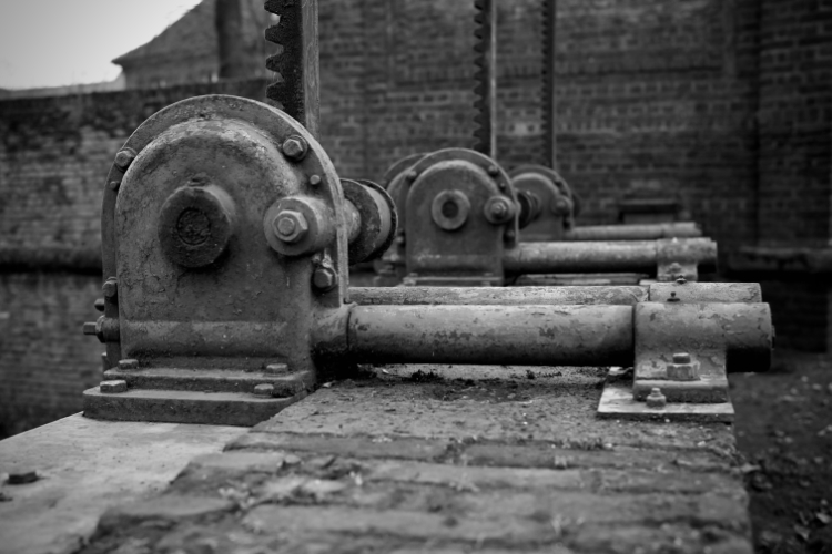 Black-and-white close-up image of a rusty mechanical component of the Düsseldorf Spee'scher Graben water control structure, sharply focused in the foreground.