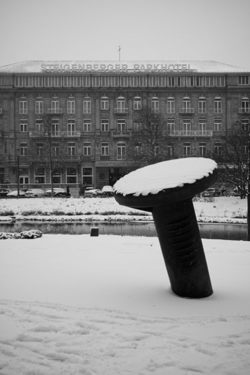 Black and white photo of a snow-covered sculpture by Günther Uecker in a winter landscape in front of the Steigenberger Parkhotel in Düsseldorf.