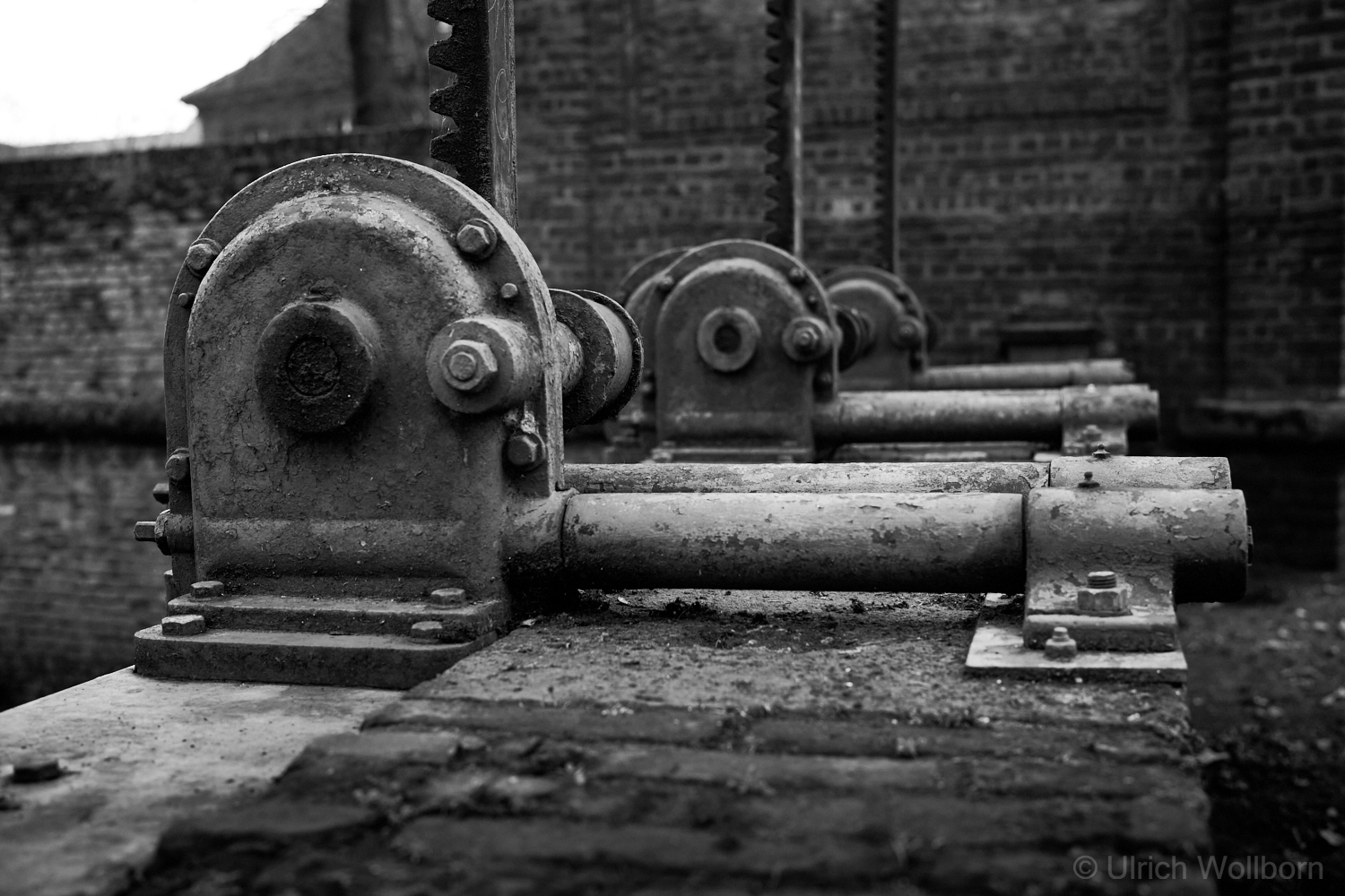 Black-and-white close-up image of a rusty mechanical component of the Düsseldorf Spee'scher Graben water control structure, sharply focused in the foreground.
