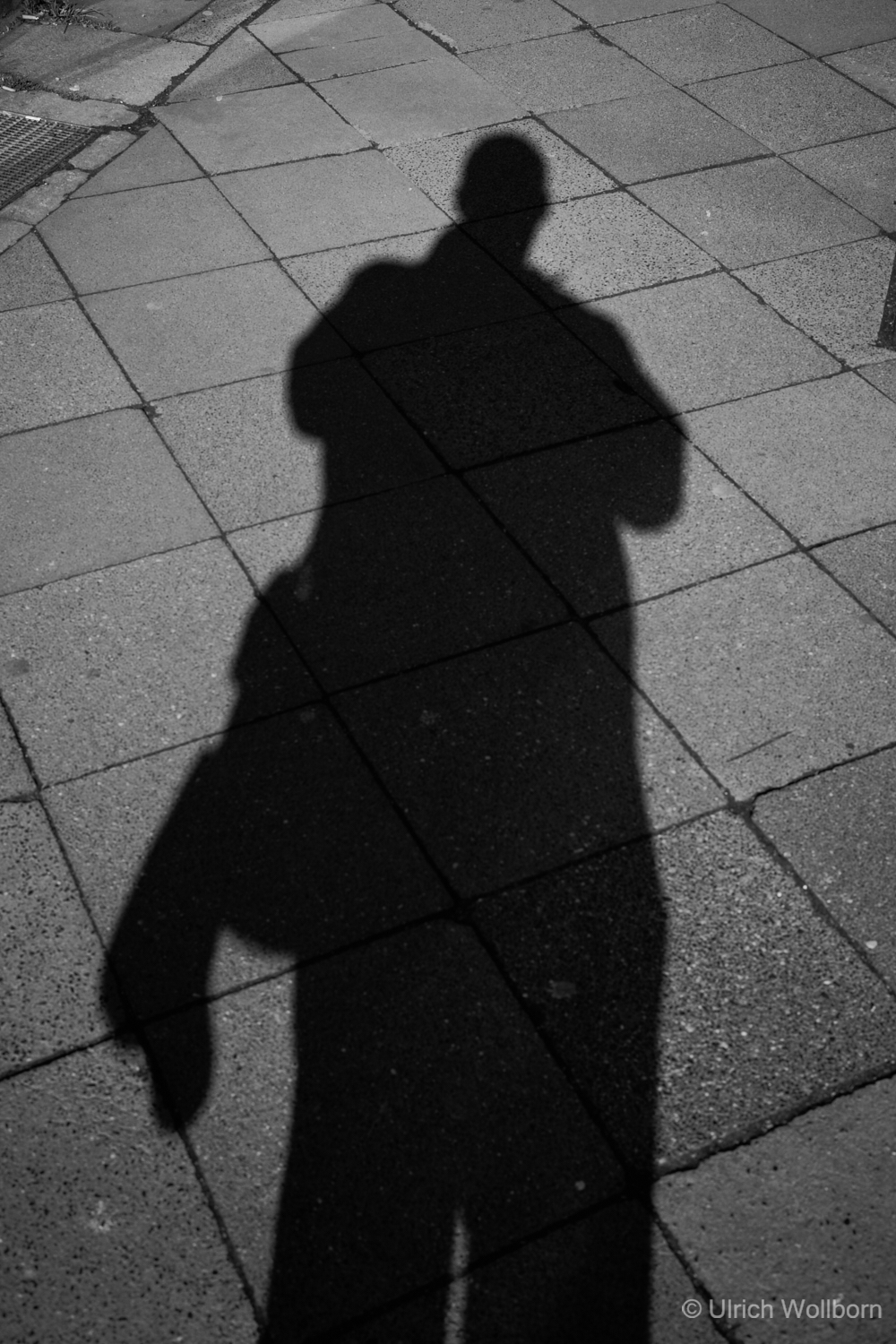 Shadow photograph on a paved sidewalk: The shadow of the photographer Ulrich Wollborn is visible.