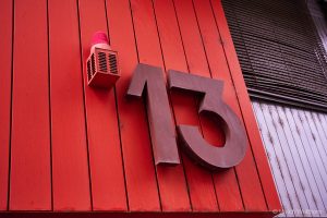 Close-up of a bold red wooden wall featuring a large brown number 13 and a red warning light above it.